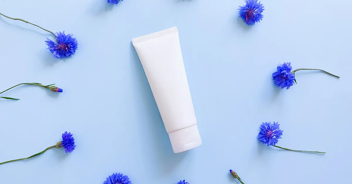An unbranded tube of ointment surrounded by blue fruit on a blue background.