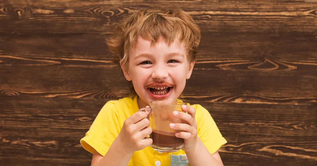 Smiling young boy enjoys a glass mug of delicious chocolate milk.