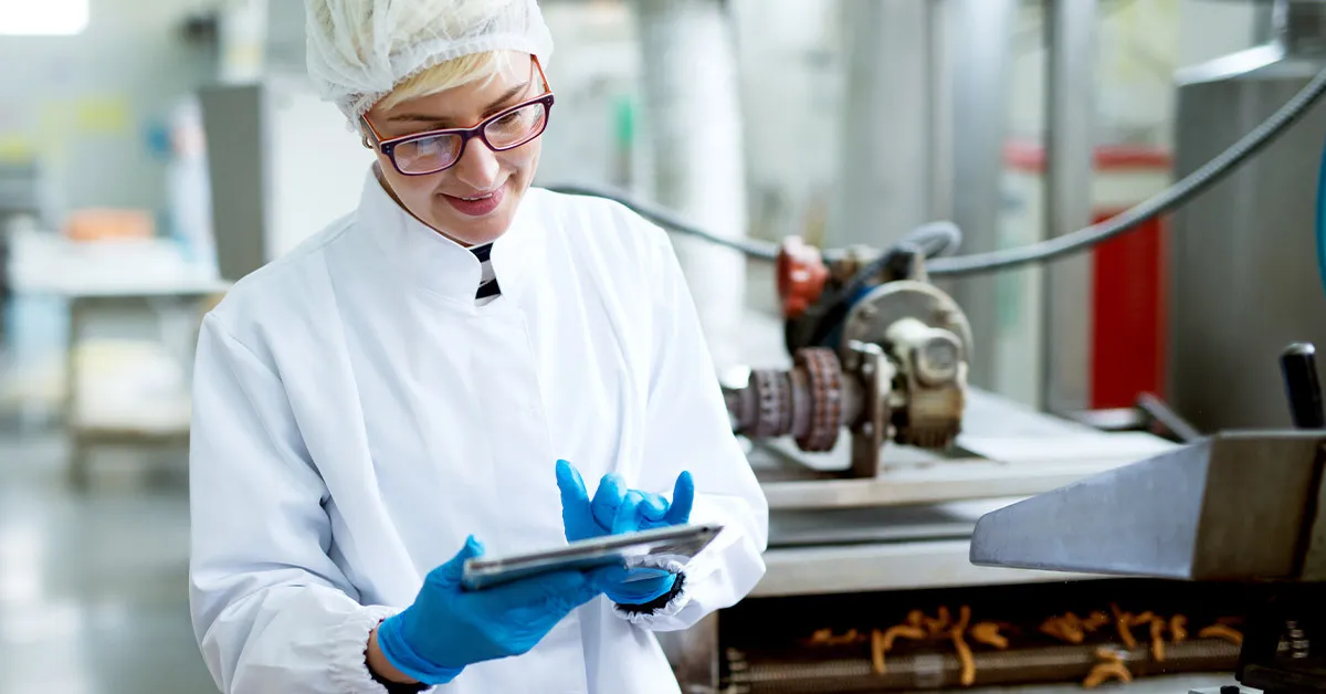 Women with tablet records updates on food quality control data in a processing plant.
