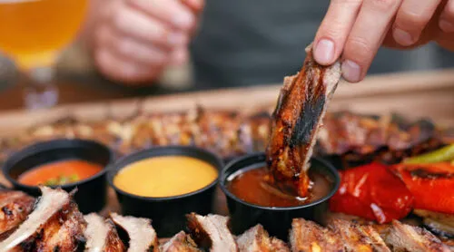 A diner dips ribs in BBQ sauce.