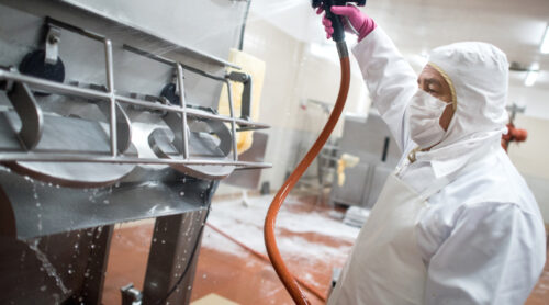 A person wearing protective clothing cleans industrial machinery.